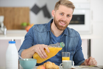 happy young man pouring orange juice - obrazy, fototapety, plakaty