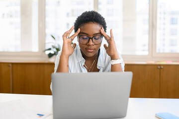 Concentrated african-american female employee colleague sitting on the workplace in front of laptop...