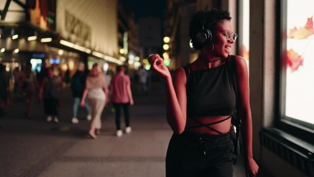 Happy black female dancing and singing with music, woman forms heart with hands symbolizing friendship and love amidst hustle of city life, humanity's universal language of kindness. Slow motion
