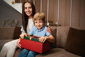 Smiling woman sitting with her son giving New Year gift celebrating Christmas