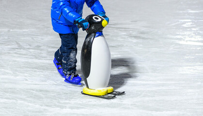Boy in warm clothes  learning ice skating with helper on ice rink. Winter day at the skating rink.