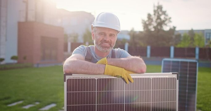 Caucasian man working at renewable energy enterprise. Professional contractor leaning at solar panel and smiling. Male technician engineer installing solar panels. Alternative enersy source.