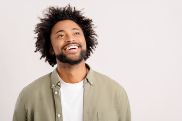 Studio photo of happy young african-american guy wearing white casual t-shirt posing isolated on white background. Smiling millennial man looking up