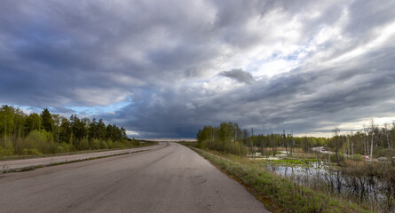 Abandoned highway. spring landscape with a cloudy sky and a highway, a swampy roadside area, environmental disruption due to the construction of a highway.