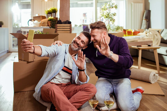 Carefree gay couple having video call in new home