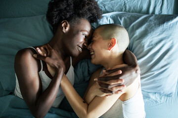 Young lesbian couple smiling and holding hands in bed