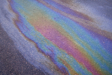 Background texture of an oil spill in the form of a rainbow stain on dark asphalt, parking
