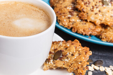 Cup of white coffee and fresh baked oatmeal cookies with honey and healthy seeds. Delicious crunchy dessert