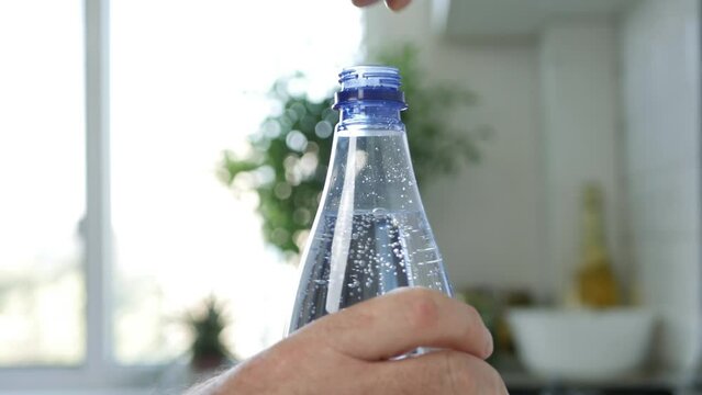 Blurred Shooting with a Thirsty Man Opening the Cap of a Plastic Bottle Full with With Cold Mineral Water and Bubbles. 