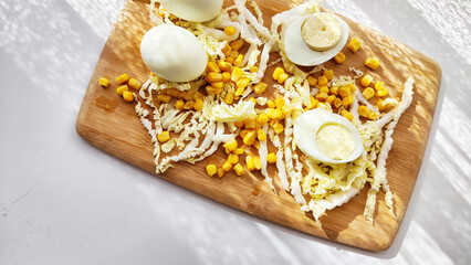 Fototapeta na wymiar Chopped Peking cabbage, peeled eggs and yellow canned corn on cutting board as a background. Cooking a healthy eco-friendly salad from natural products. Copy space and place for text