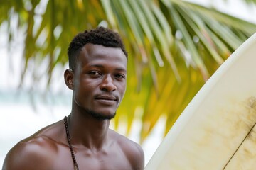 Relaxed studio portrait of a young African man in beachwear, with a surfboard, isolated on a tropical beach background
