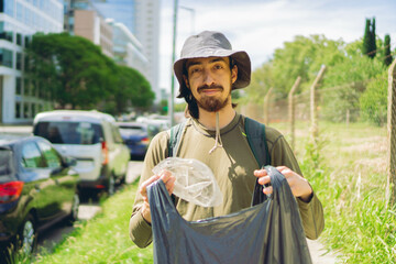 young Latin man smiles at camera while cleaning trash from city green spaces with garbage bag