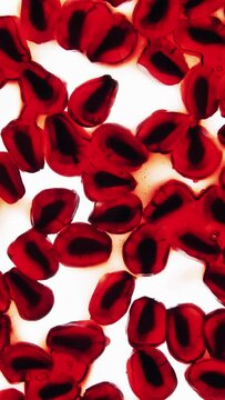 Vertical crushing and squeezing lot of red pomegranate fruit seeds. Crush juicy berries creating juice and pulp splash on clean white background. Squeeze fresh pomegranate. Food style shooting	