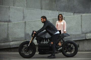 fashion couple sitting on a motorcycle, stone wall on the background. young man and woman with...