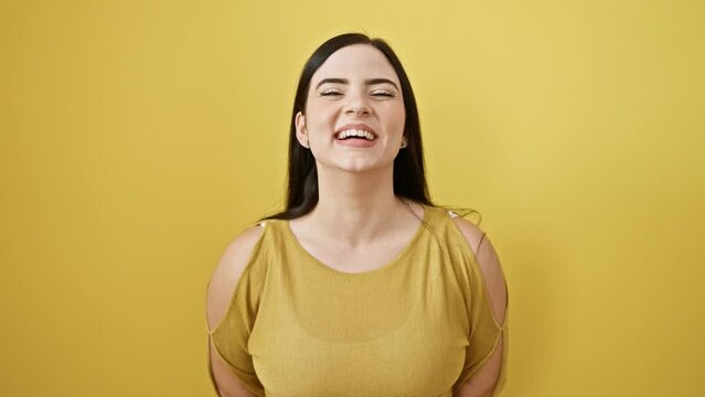 Hilarious shot of young, beautiful hispanic woman making a funny face, puffing up inflated cheeks catching air. standing person amused, eyes full of joy, against isolated yellow background.