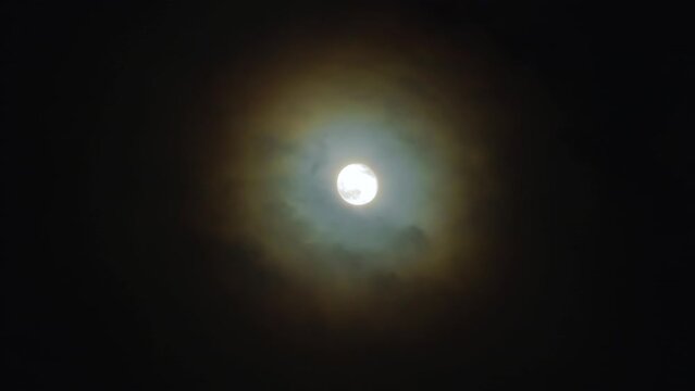 Full moon in the night sky. The corona is a light optical phenomenon in the form of colored clouds around the Moon on a dark, cloudy night