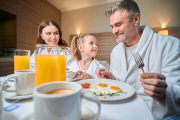 Mother and daughter looking at father during having breakfast in hotel room