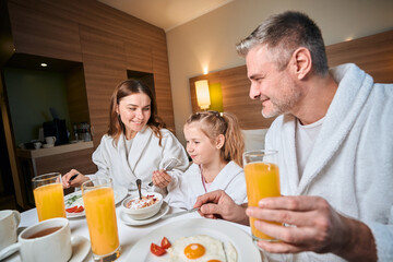 Fototapeta na wymiar Father looking at mother feeding daughter flakes during having breakfast in room