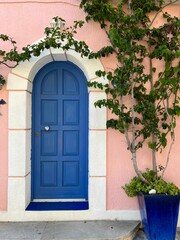 Fototapeta na wymiar Blue wooden door in an arched doorway of a pink house, Assos village, Kefalonia island, Greece