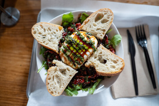 delicious ball of buratta cheese covered in pesto and oil surrounded by bread toast on top of a salad at italian restaurant