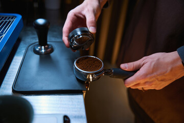 Barista holding portafilter and coffee tamper making espresso coffee in cafe