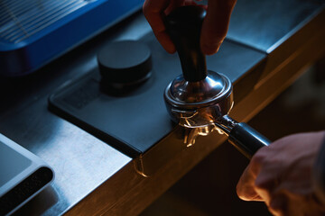 Barista holding portafilter and coffee tamper making espresso coffee