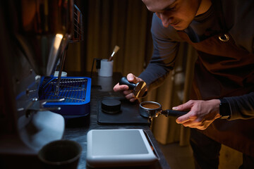 Barista holding portafilter with grinded coffee and tampering in coffee shop