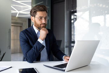 Serious young businessman is working concentratedly in the office on a laptop and with documents