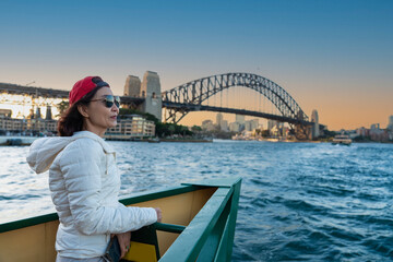 Asian female tourist carries a backpack on a boat trip to see the Sydney Harbor, seeing the Sydney Harbor Bridge in the evening, Australia.