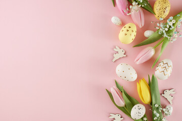 Creating a happy easter atmosphere. Top view photo of colorful eggs, fresh flowers, easter bunnies on pastel pink background with promo area
