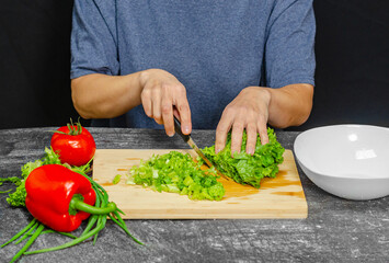 Female hands cut green lettuce leaves on cutting board with knife for preparing vegetarian food.