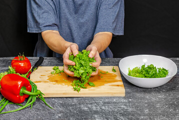 Green salad leaves in hands near white bowl. Blue t-shirt, black background. Bright vegetables.