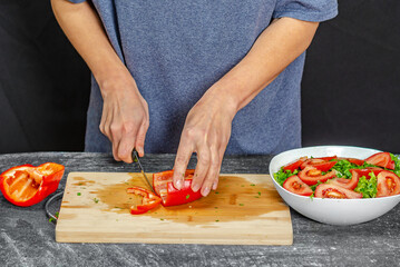 Female hands cutting pepper on cutting board. Blue t-shirt, black background. Salad preparation.
