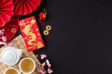 Discovering the traditions of the chinese New Year tea ritual. Top view photo of tea crockery, money envelope, traditional chinese decor on black background with promo space