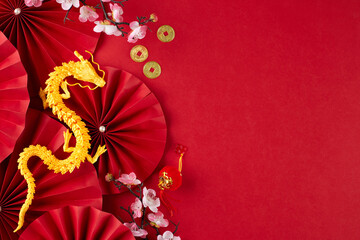 Respecting and upholding the traditions of a Chinese New Year. Top view photo of gold dragon, folding fans, sakura bloom, traditional coins on red background with promo space