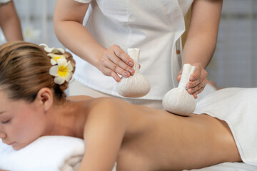 Hot herbal ball spa massage body treatment, masseur gently compresses herb bag on woman body....