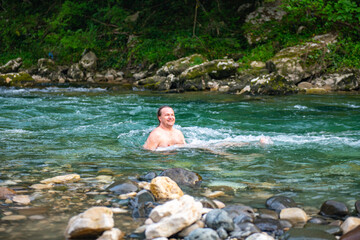 Man with Long Hair Finding Serenity while Swimming in a Scenic Mountain River with Trees and Rocks
