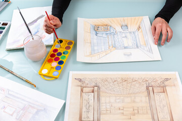 Interior designer is dipping a brush in yellow paint, and working on color hand drawing of living...