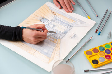 Close up interior designer's hands which are working on color hand drawing of cosy room using a pencil.