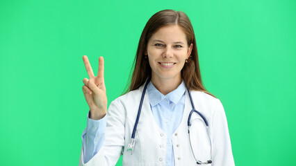 Female doctor, close-up, on a green background, shows a victory sign