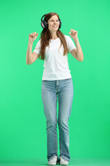 A woman, full-length, on a green background, wearing headphones