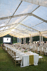 
Long table setting with beautiful flower arrangements for intimate wedding or party-outdoors family gathering on sunny day under transparent tent
