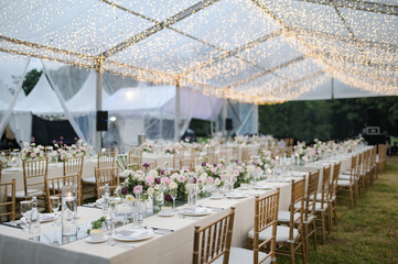 
Long table setting with beautiful flower arrangements for intimate wedding or party-outdoors family gathering on sunny day under transparent tent

