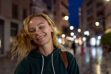 portrait of a girl with blond hair in a green jacket, the girl stands on the street in the evening