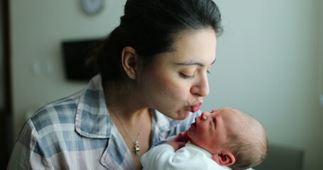 Mother holding newborn baby kissing infant, showing love after birth