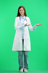 A full-length female doctor, on a green background, points to the side