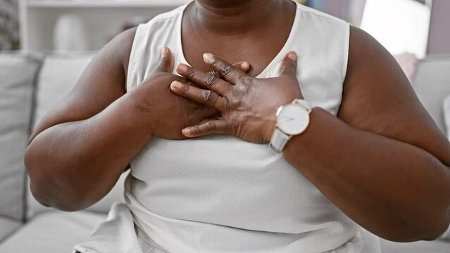A grateful african american woman, hands on chest, feeling positive emotions of hope and care at home, breathing calm amidst heart health concerns