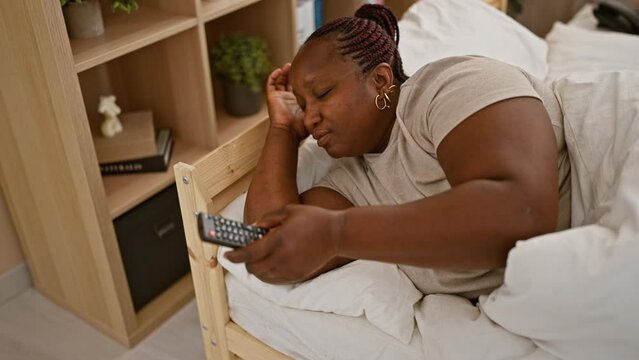 African american woman watching tv lying on bed at bedroom