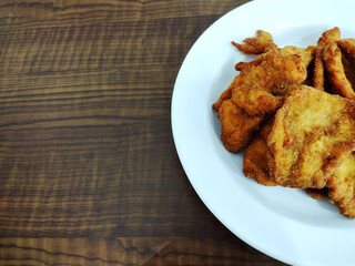 Parial view  of portion of breaded chicken breast on the wooden table.
