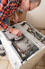 gray-haired man The owner is a jack of all trades who can check a broken washing machine himself, detect the breakdown and repair it, high quality photo
